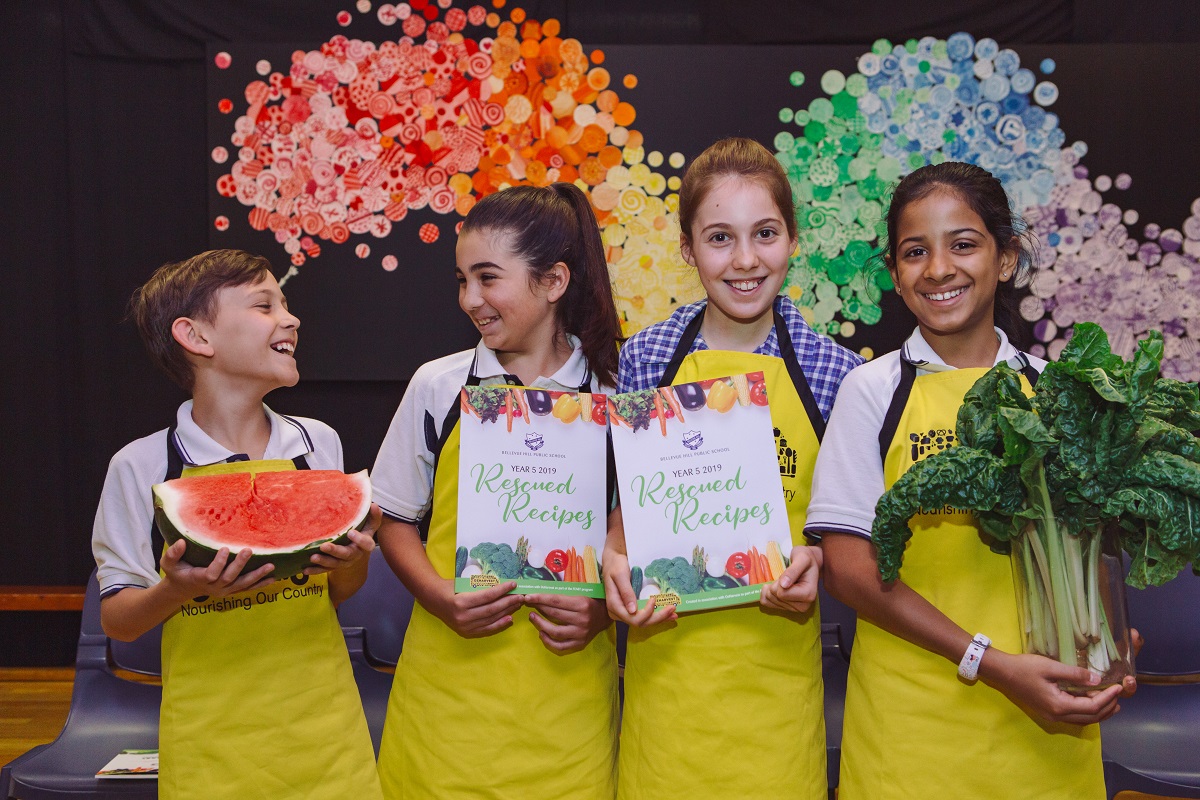 Four OzHarvest FEAST students - the boy is holding a watermelon, two girls holding cookbooks and another girl holding silverbeet