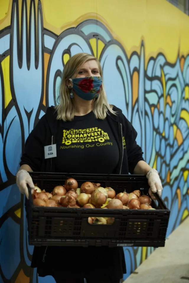 Eliza wearing a mask at OzHarvest Market in Waterloo holding a crate of onions