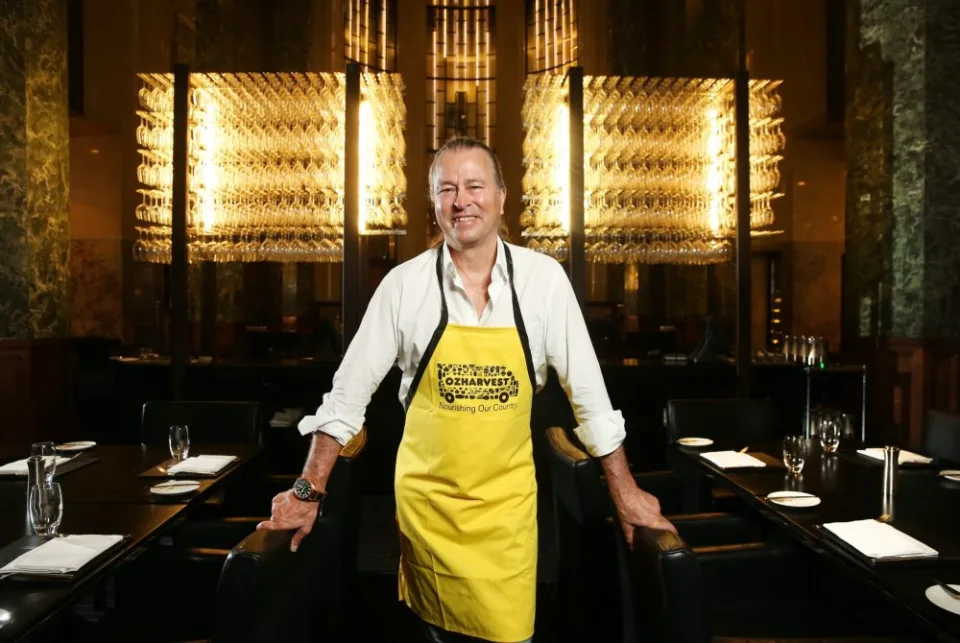 Chef Neil Perry smiling at his restaurant wearing the ozharvest yellow apron