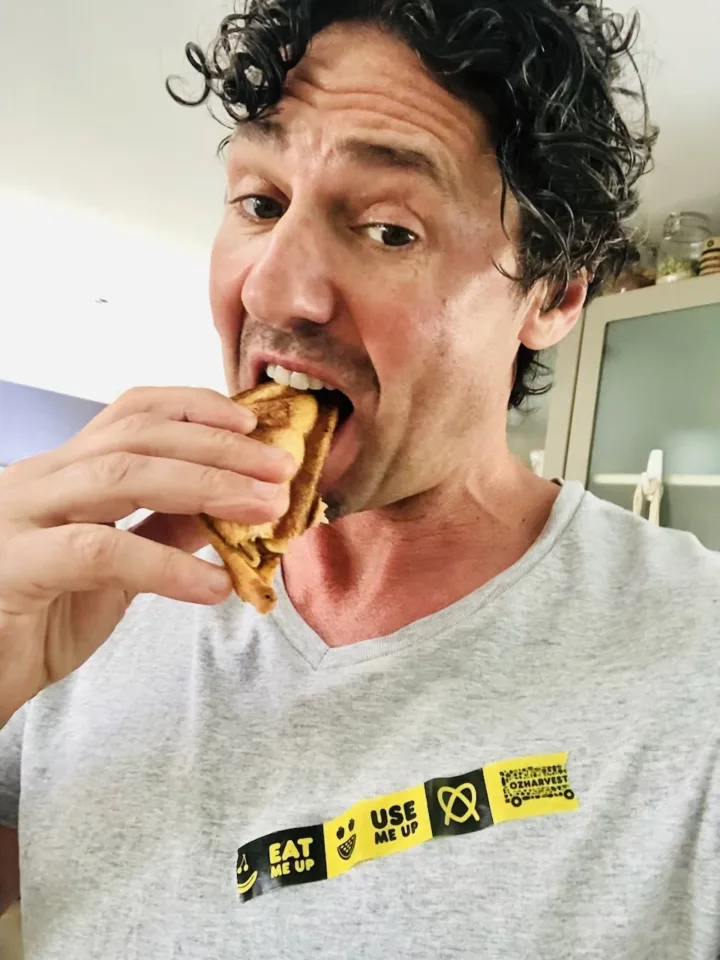 Chef Colin Fassnidge eating a sandwich wearing a grey shirt with the use It up tape on it