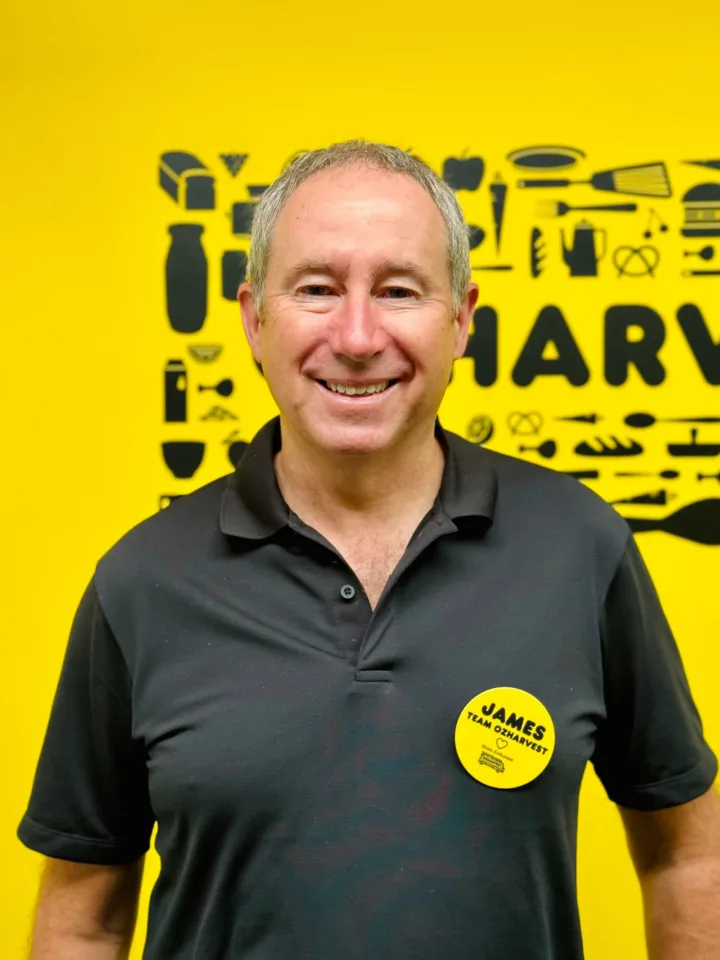 OzHarvest CEO James Goth smiling in front of a yellow wall.
