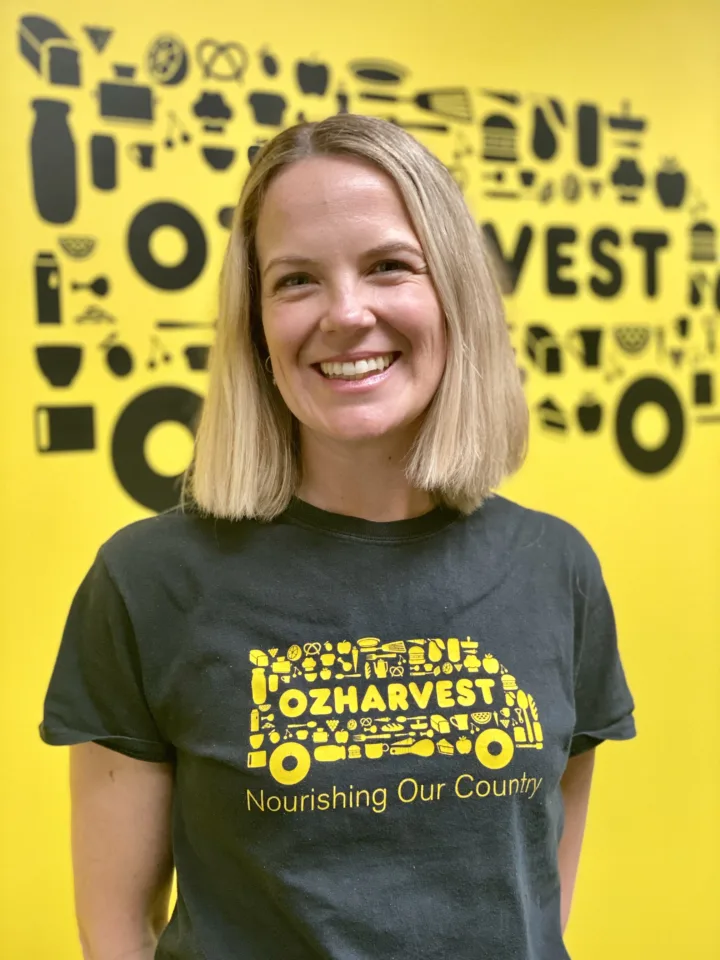 OzHarvest Head of Impact Laura Glendinning smiling smiling in front of a yellow wall.