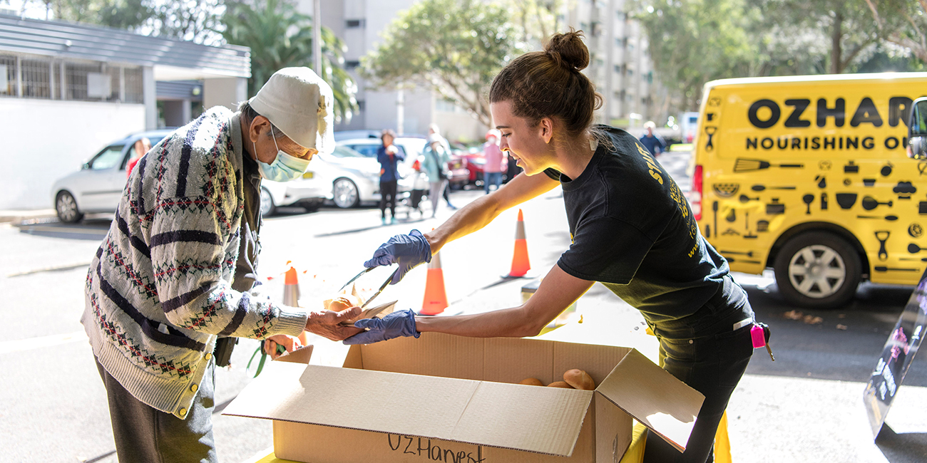A younger ozharvest volunteer providing free bread to an elderly lady